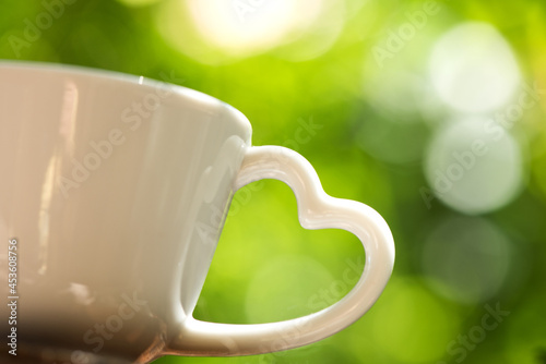 Foto Heart-shaped coffee cup handle on bokeh natural background.