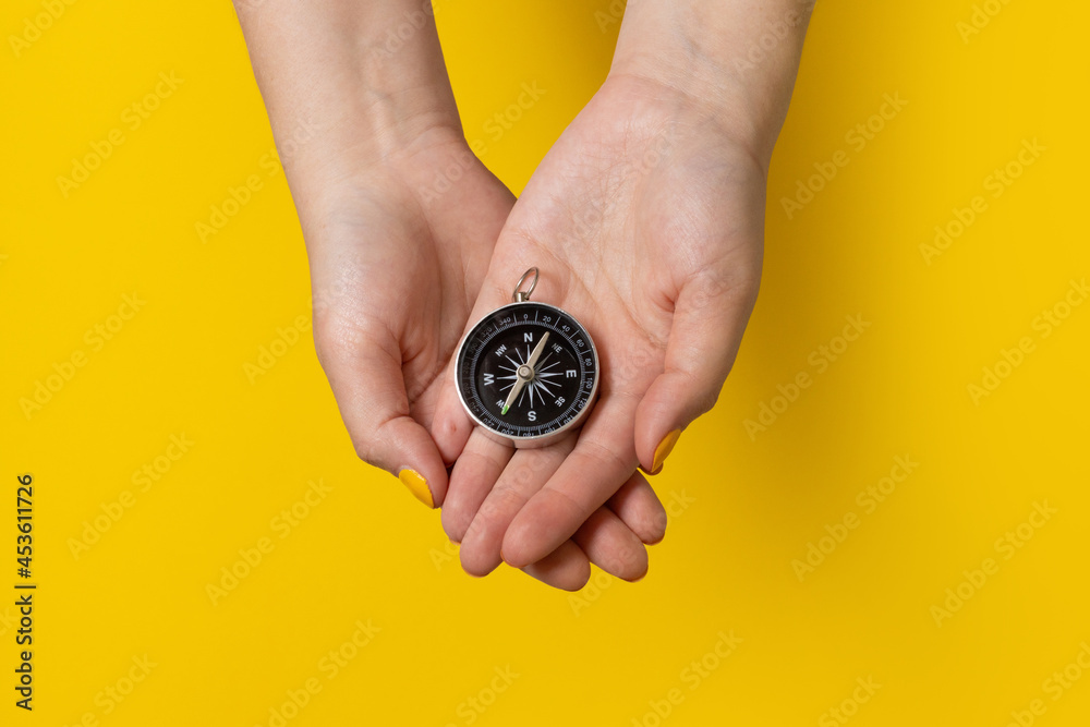 Close-up female hands holding a compass on a yellow background. Travel lifestyle, summer vacation concept Close-up female hands holding a compass on a yellow background. Travel lifestyle, summer vacation concept