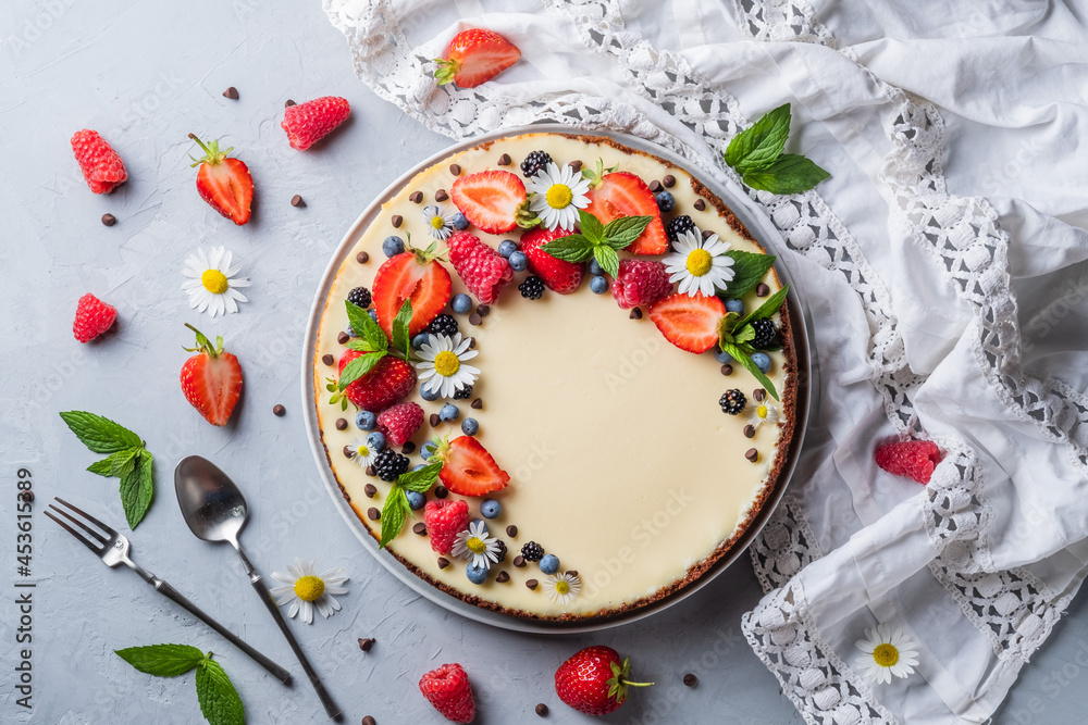 Cheesecake pie with fresh berries, strawberries, blueberries and blackberries and mint chamomiles in a round plate on a grey background. Cheesecake pie with fresh berries, strawberries, blueberries and blackberries and mint chamomiles in a round plate on a grey background.