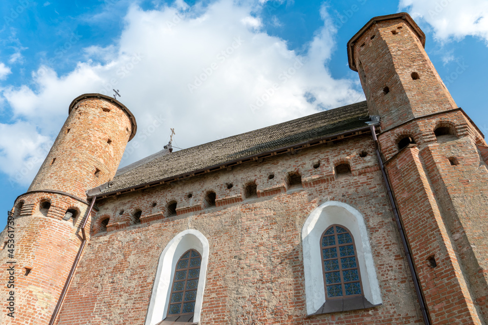 A beautiful old fortress church made of red brick against a blue sky background. A high impregnable fortress with iron crosses on the domes, arched windows and an icon in the center of the wall.