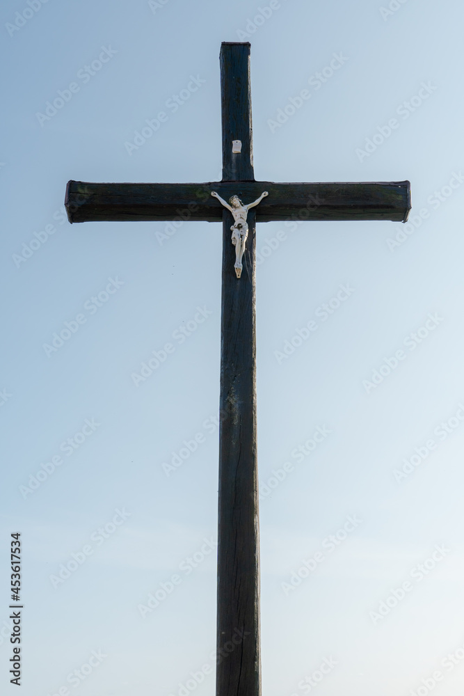 An old wooden Christian cross against a clear blue sky on a beautiful summer day. A statuette of Jesus in the center of the cross. The crucifixion of Christ. The feast of Easter and Resurrection.