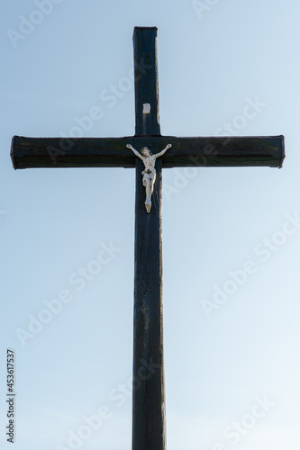 An old wooden Christian cross against a clear blue sky on a beautiful summer day. A statuette of Jesus in the center of the cross. The crucifixion of Christ. The feast of Easter and Resurrection.