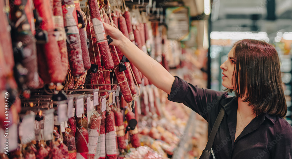 Young woman chooses salami sausage in a supermarket