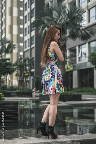 Lovely asian woman in casual colourful dress standing outdoors near modern building. Long hair. Nice posture. High quality photo 