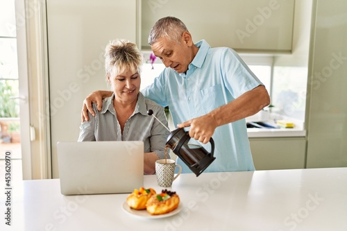 Senior caucasian couple having breakfast using laptop at the kitchen.