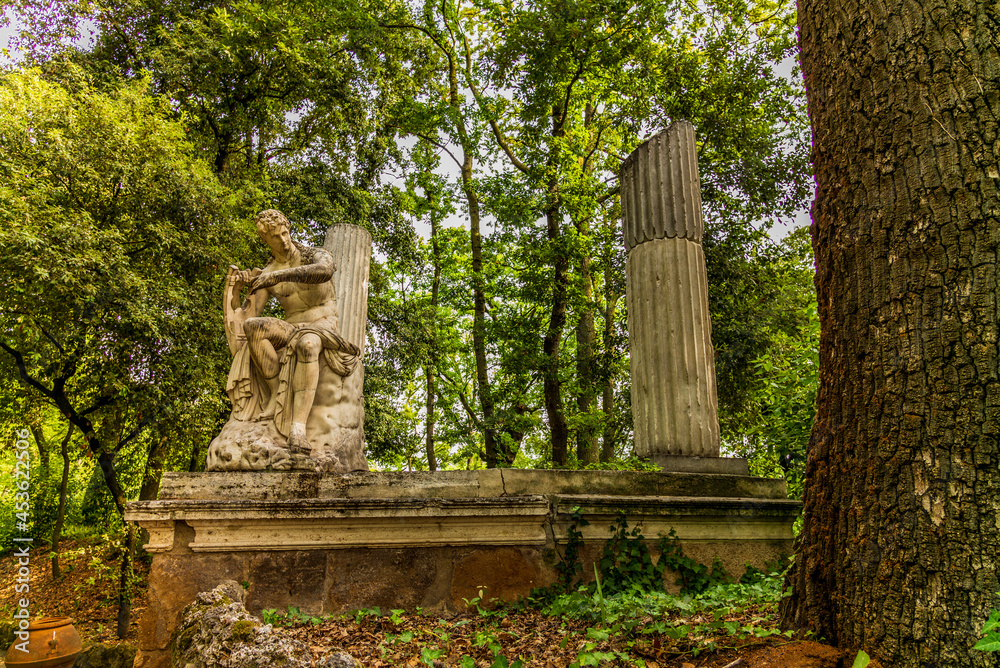 A path in a garden in Rome with old statues, columns, and water fountains