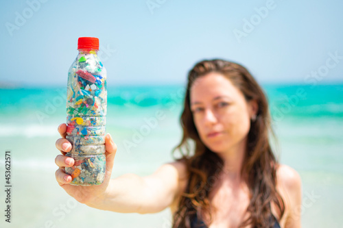 Caucasian woman holding a bottle filled with microplastics collected from the beach.