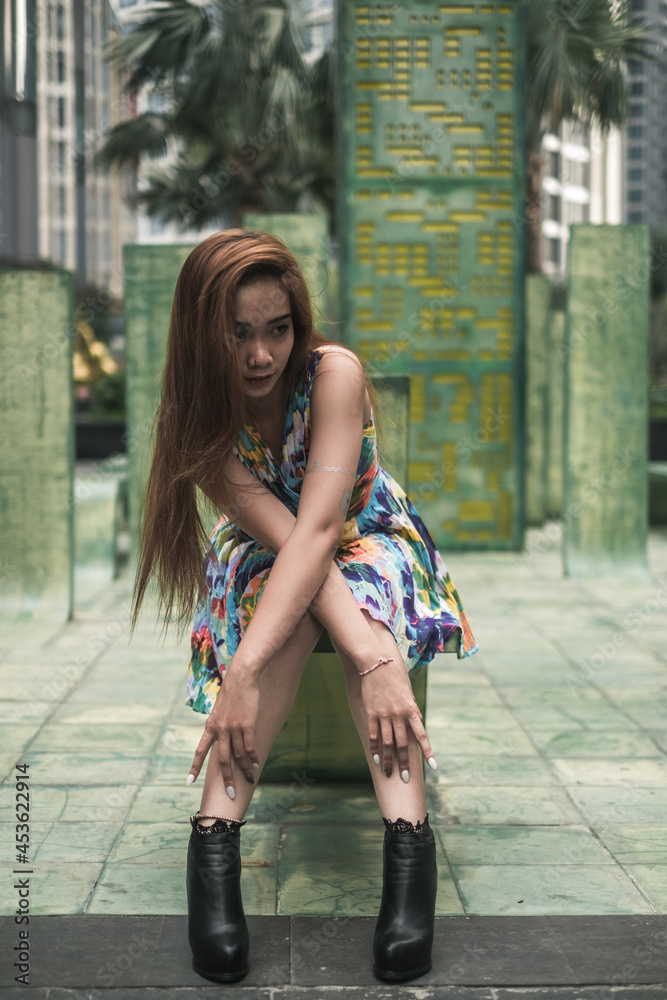 Lovely asian woman in casual colourful dress sitting outdoors near modern buildings. Urban concept. Long hair. Nice posture. High quality photo 