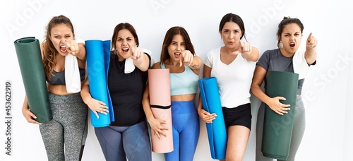 Group of women holding yoga mat standing over isolated background pointing displeased and frustrated to the camera, angry and furious with you