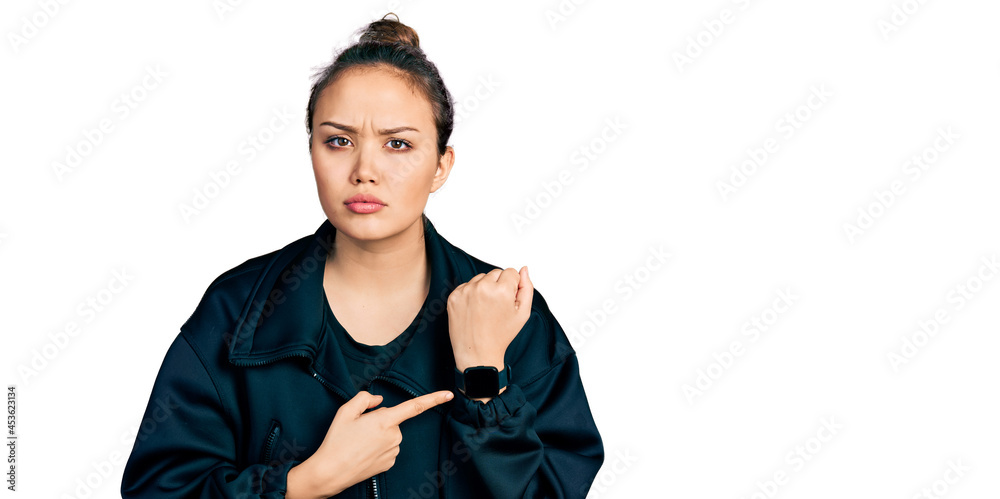 Young hispanic girl wearing sportswear in hurry pointing to watch time, impatience, looking at the camera with relaxed expression Young hispanic girl wearing sportswear in hurry pointing to watch time, impatience, looking at the camera with relaxed expression