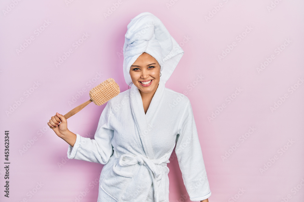 Young hispanic girl wearing bathrobe holding sponge looking positive and happy standing and smiling with a confident smile showing teeth