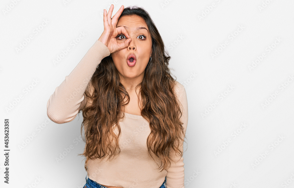 Young hispanic girl wearing casual clothes doing ok gesture shocked with surprised face, eye looking through fingers. unbelieving expression. Young hispanic girl wearing casual clothes doing ok gesture shocked with surprised face, eye looking through fingers. unbelieving expression.