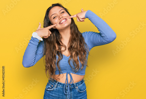 Young hispanic girl wearing casual clothes smiling cheerful showing and pointing with fingers teeth and mouth. dental health concept.