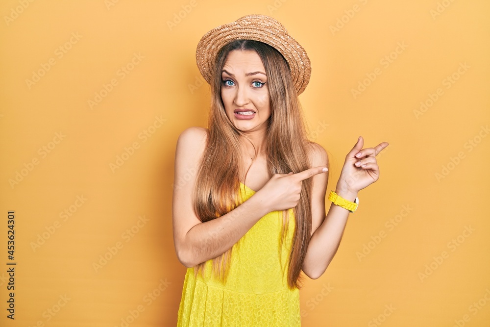 Young blonde girl wearing summer hat pointing aside worried and nervous with both hands, concerned and surprised expression Young blonde girl wearing summer hat pointing aside worried and nervous with both hands, concerned and surprised expression