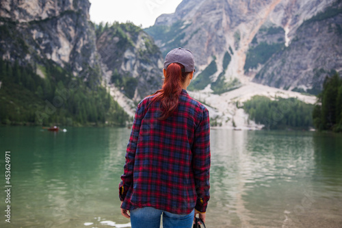 young girl tourist in a plaid shirt and cap standing in front of the lago di Braies in the Dolomites of South Tyrol. Tourism direction to northern Italy. Bolzano Lago di Braies Italy