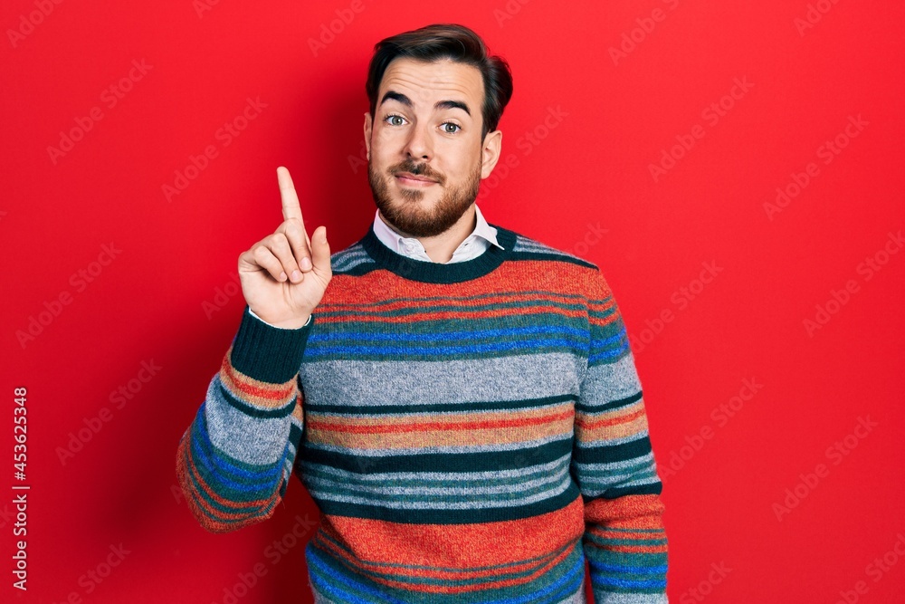 Naklejka premium Handsome caucasian man with beard wearing elegant wool winter sweater showing and pointing up with finger number one while smiling confident and happy.
