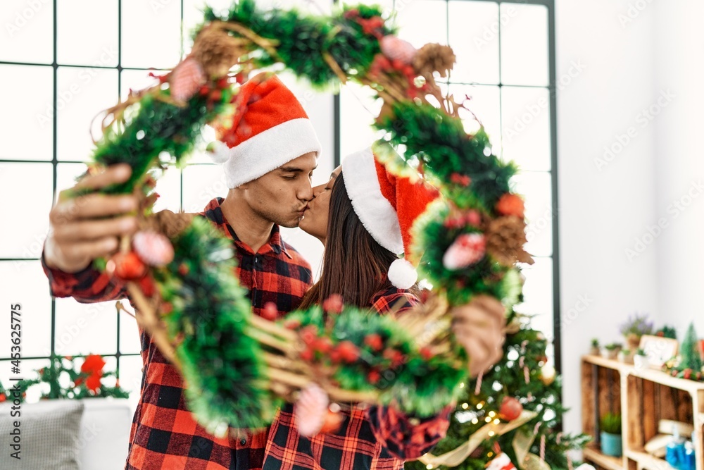 Young latin couple kissing and holding christmas decor at home.