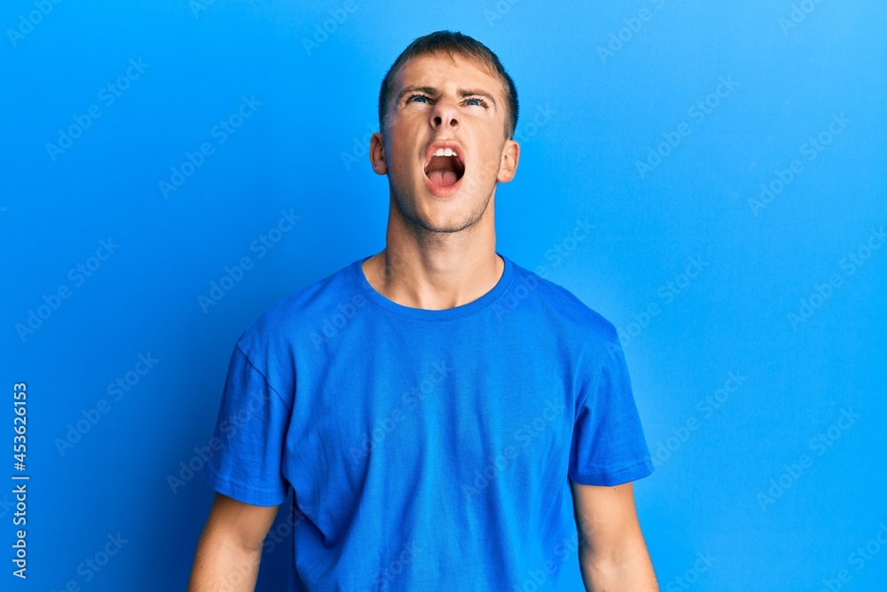 Young caucasian man wearing casual blue t shirt angry and mad screaming frustrated and furious, shouting with anger. rage and aggressive concept. Young caucasian man wearing casual blue t shirt angry and mad screaming frustrated and furious, shouting with anger. rage and aggressive concept.