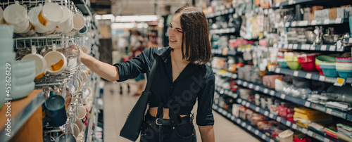 Shopping yong woman looking at the shelves with cup in supermarket.