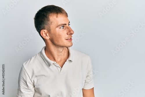 Young caucasian man wearing casual white polo looking to side, relax profile pose with natural face and confident smile.