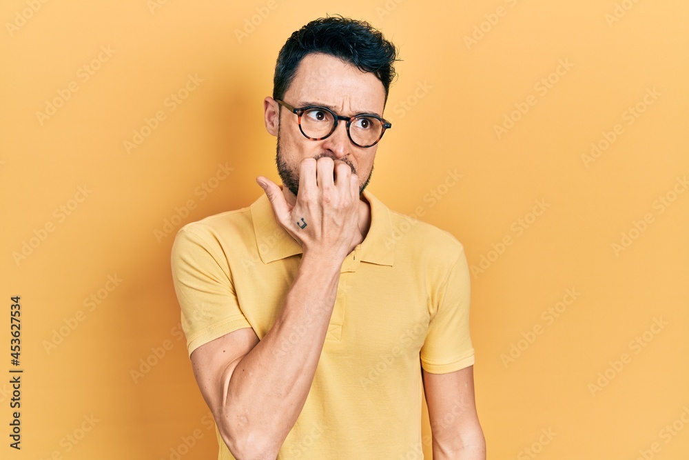 Young hispanic man wearing casual clothes and glasses looking stressed and nervous with hands on mouth biting nails. anxiety problem. Young hispanic man wearing casual clothes and glasses looking stressed and nervous with hands on mouth biting nails. anxiety problem.