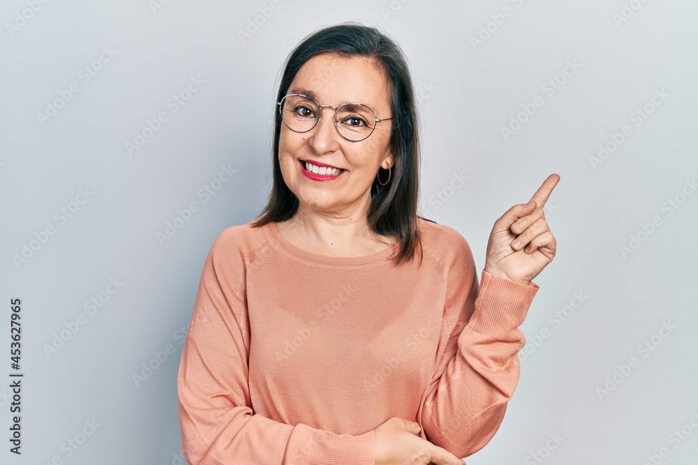 Middle age hispanic woman wearing casual clothes and glasses smiling happy pointing with hand and finger to the side Middle age hispanic woman wearing casual clothes and glasses smiling happy pointing with hand and finger to the side