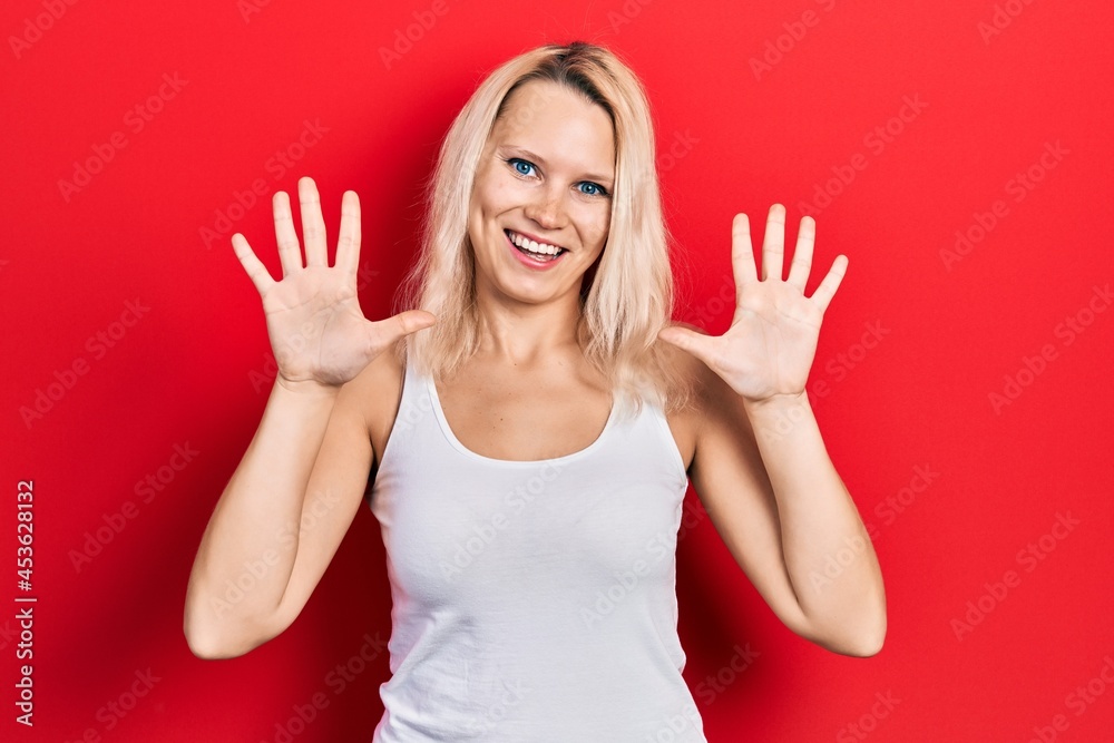 Fototapeta premium Beautiful caucasian blonde woman wearing casual white t shirt showing and pointing up with fingers number ten while smiling confident and happy.