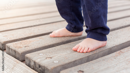 Kind steht Barfuß auf Holzbrettern. Natürliche Terrassendielen. Child stands barefoot on wooden boards. Natural decking.