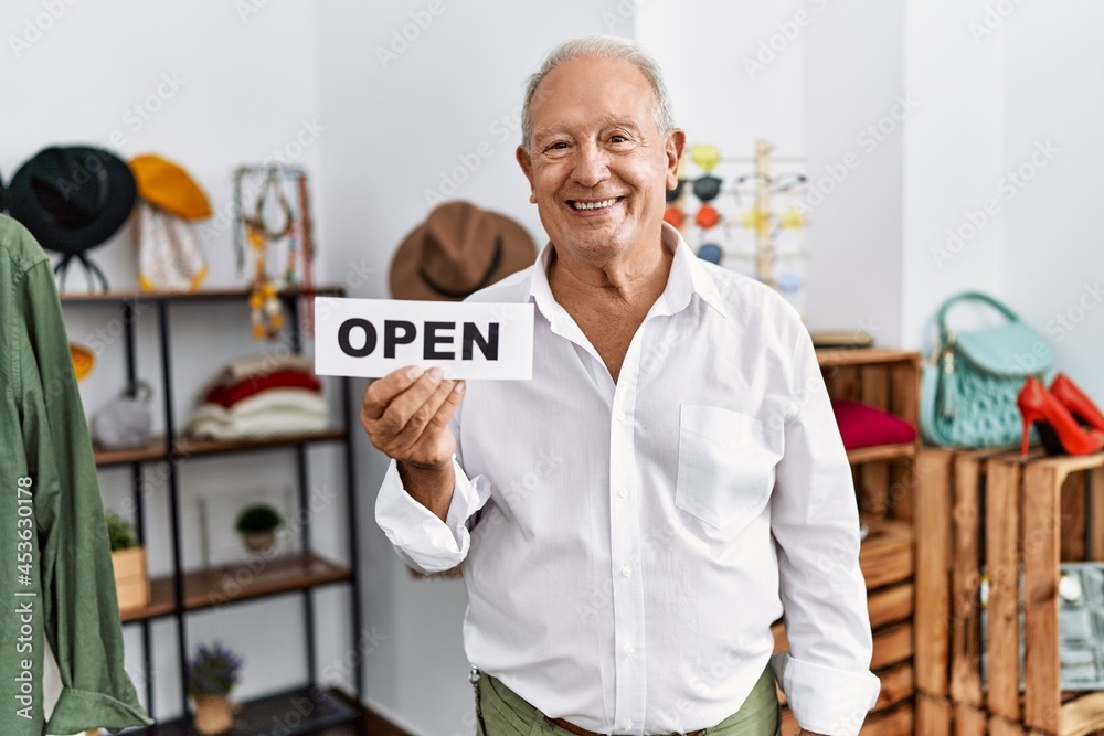 Senior man holding banner with open text at retail shop looking positive and happy standing and smiling with a confident smile showing teeth