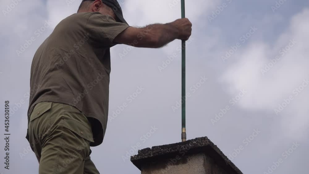 The man on the roof makes measured movements with the brush in the chimney for cleaning.
