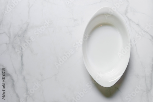 Empty white oval bowl isolated on white marble background; top view and copy space.