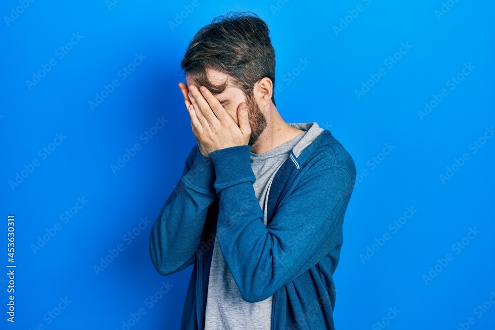 Caucasian man with beard wearing casual sweatshirt with sad expression covering face with hands while crying. depression concept. Caucasian man with beard wearing casual sweatshirt with sad expression covering face with hands while crying. depression concept.