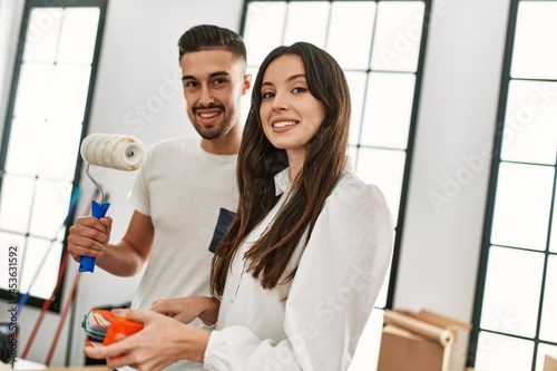Young hispanic couple painting using paint roller at new home.