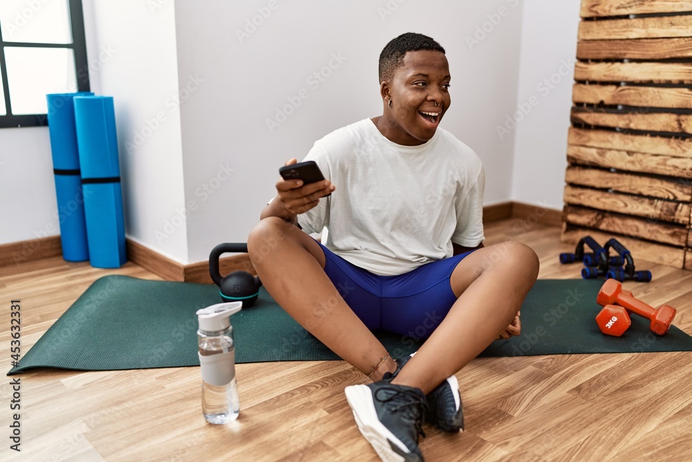 Young man sitting on training mat at the gym using smartphone Young man sitting on training mat at the gym using smartphone