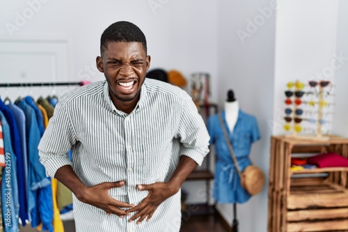 Young african american man working as manager at retail boutique with hand on stomach because indigestion, painful illness feeling unwell. ache concept.