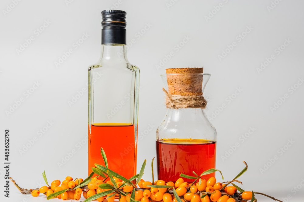 Two bottles of sea buckthorn oil and a bush of fresh sea buckthorn berries on a white background Two bottles of sea buckthorn oil and a bush of fresh sea buckthorn berries on a white background