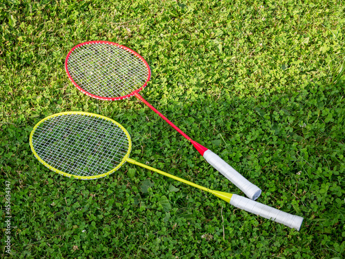 Two simple colorful badminton rackets laying on the grass, closeup, nobody. Leisure, sports recreation equipment symbol, healthy summer outdoor activities, entertainment accessories abstract concept