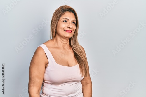 Middle age hispanic woman wearing casual style with sleeveless shirt looking away to side with smile on face  natural expression. laughing confident.