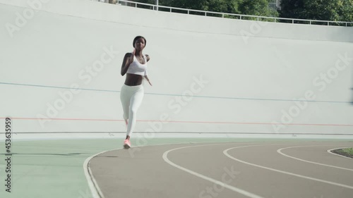Confident young African woman in sports clothing running on track outdoors