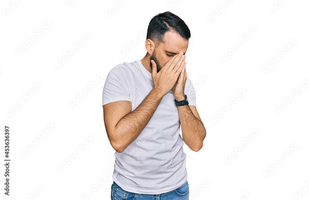 Young man with beard wearing casual white t shirt with sad expression covering face with hands while crying. depression concept. Young man with beard wearing casual white t shirt with sad expression covering face with hands while crying. depression concept.