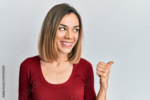 Young caucasian blonde woman wearing casual jumper pointing thumb up to the side smiling happy with open mouth