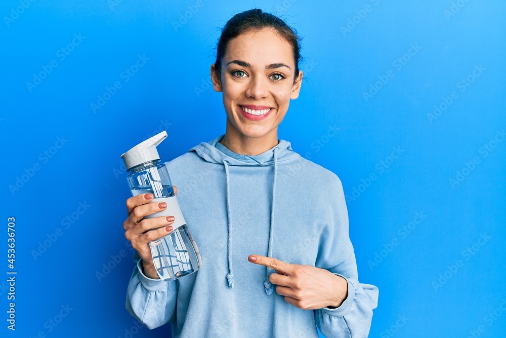 Young caucasian blonde woman drinking bottle of water smiling happy pointing with hand and finger Young caucasian blonde woman drinking bottle of water smiling happy pointing with hand and finger
