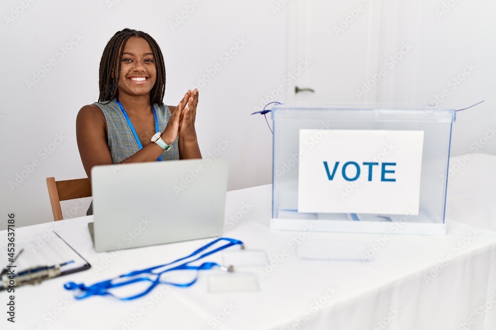 Young african american woman working at political election sitting by ballot clapping and applauding happy and joyful, smiling proud hands together Young african american woman working at political election sitting by ballot clapping and applauding happy and joyful, smiling proud hands together
