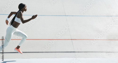 Beautiful young African woman in sports clothing running on track outdoors