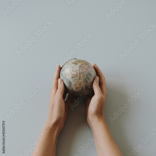 Globe model in female hands on blue background. Save the world, planet Earth concept. Women's rights and power concept