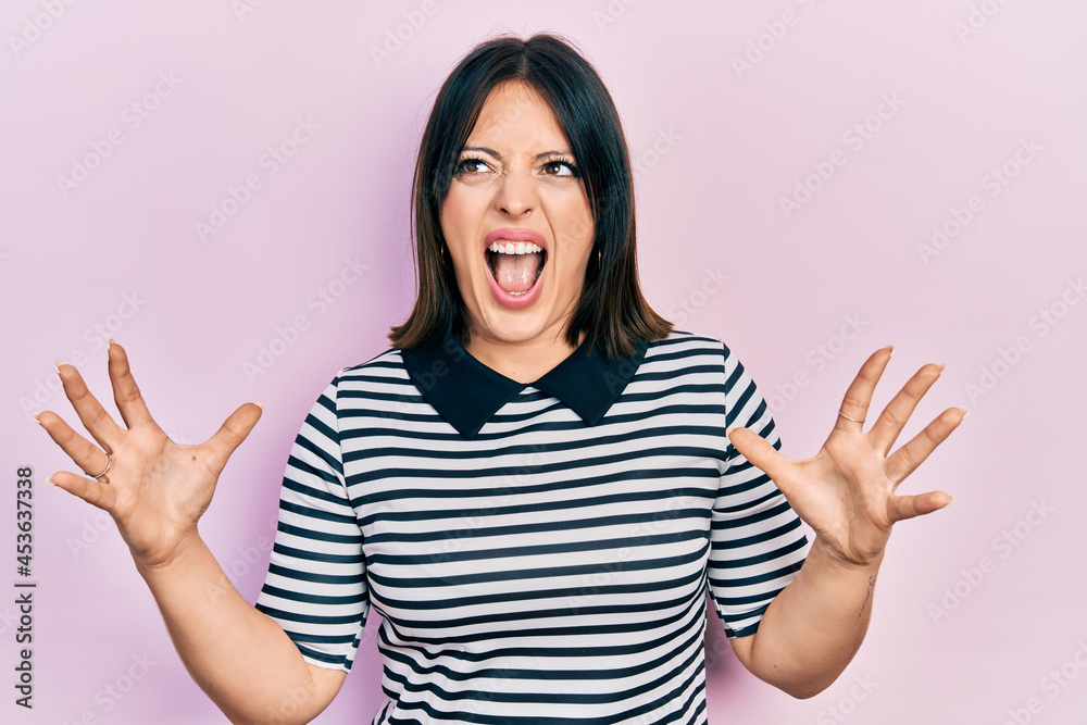 Young hispanic woman wearing casual clothes crazy and mad shouting and yelling with aggressive expression and arms raised. frustration concept. Young hispanic woman wearing casual clothes crazy and mad shouting and yelling with aggressive expression and arms raised. frustration concept.