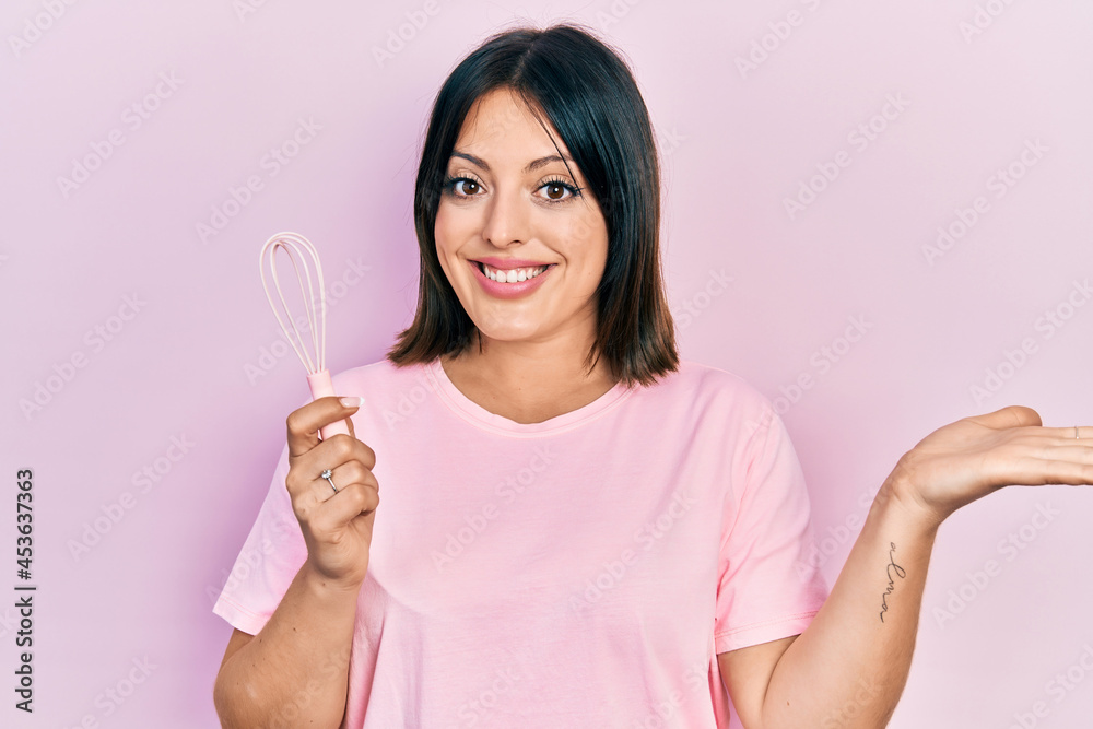 Young hispanic woman cooking using baker whisk celebrating achievement with happy smile and winner expression with raised hand Young hispanic woman cooking using baker whisk celebrating achievement with happy smile and winner expression with raised hand