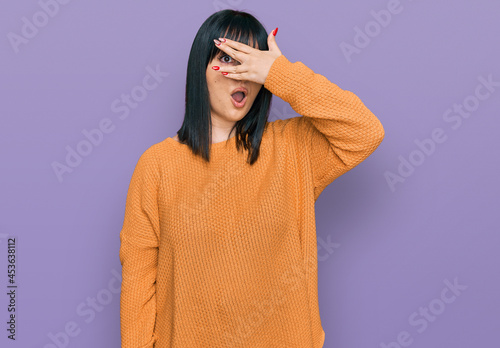 Young hispanic woman wearing casual clothes peeking in shock covering face and eyes with hand, looking through fingers with embarrassed expression.