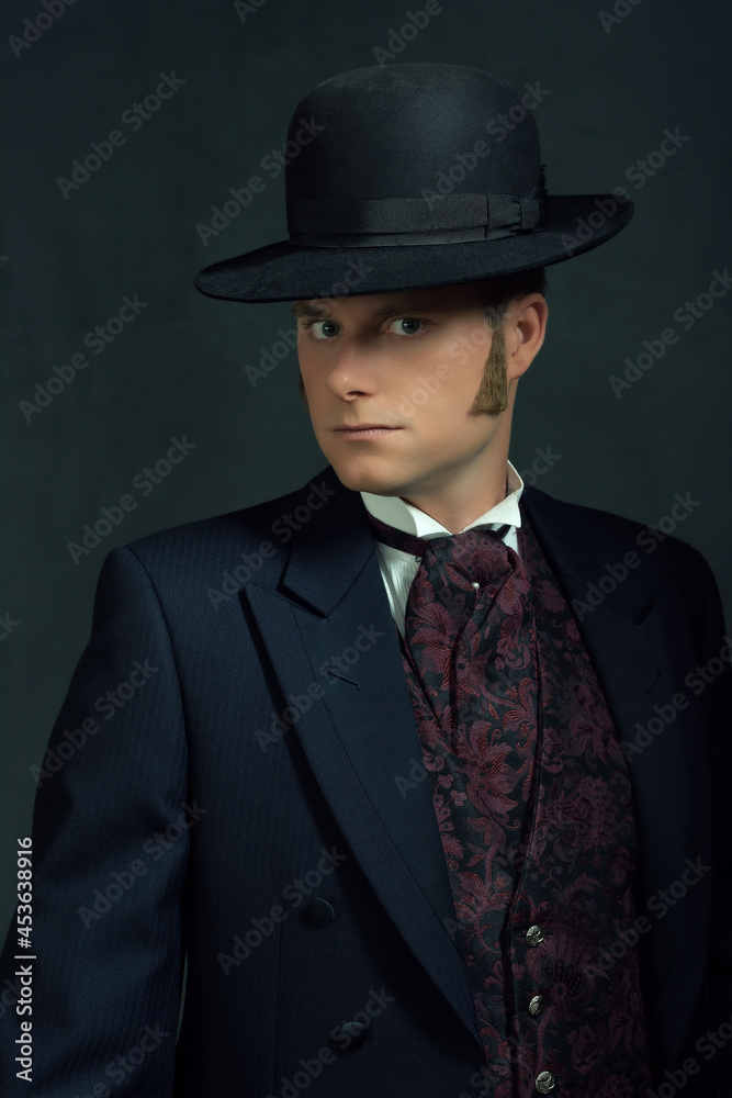 Young man in stylish vintage victorian attire. Standing in front of a dark gray wall.