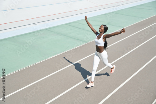 Top view of happy young African woman in sports clothing running on track and keeping arms raised © gstockstudio